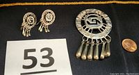 Brooch and earrings laid on black background with a penny for size comparison and lot number 53 visible.