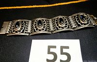 Photo of front side of the silver bracelet showing four floral contour hinged panels with oval cobalt blue stones, laid flat.