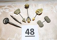 Six vintage Art Deco style hat pins displayed on a fabric background showing various shapes and styles with rhinestones and pearls.