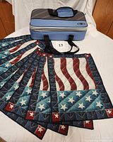 Eight American flag tapestry placemats laid out in fan shape in front of a blue and gray insulated cooler bag.