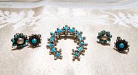 Front view of the turquoise jewelry lot showing two pairs of earrings and one horseshoe-shaped brooch with turquoise stones.