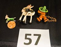 Three vintage novelty pins on black background with a penny for scale: celluloid donkey, siesta man with chain, and small metal pony pin