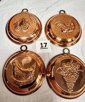 Front view of four copper molds showing embossed rooster, hen, grape cluster, and strawberry cluster.