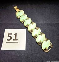 Top down photo of the entire vintage Egyptian Revival linked bracelet showing the mint green thermoset pieces and silver-tone wrap link design connected with an engraved clasp.