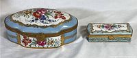 Full view of two porcelain hand-painted boxes, one larger Limoges marked and one smaller unmarked, both floral with gilt metal trim and clasps
