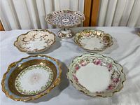Five decorative porcelain plates and bowls including a Dresden pedestal and four Limoges pieces arranged on white surface