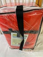Photo of one red Type Two adult universal lifejacket packed in a clear mesh/plastic bag with a black securing strap and visible instruction label.