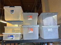 Seven clear plastic storage containers stacked on metal shelf, showing various sizes and lids.
