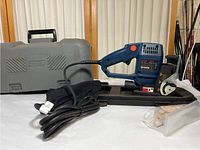 Full shot of Ryobi JM80 biscuit jointer with power cord, dust bag, plastic bag of wooden biscuits, and hard carrying case