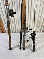 Four fishing poles standing side by side showing varying handle types and reel designs.