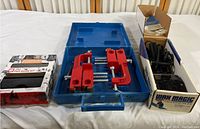 Wide shot of the lot with blue case open showing red clamps inside, Burton File Guide Kit box on left, Wax Magic waxing iron with cords and wax bars inside original box on right.