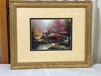 Full view of framed Thomas Kinkade print depicting stone cottage with trees and stream.