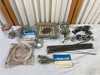 Overview of vintage bicycle parts including derailleurs, chain, spokes, hub, brake cables and other components displayed on a white surface.