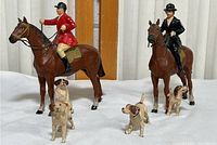 Wide shot showing two jockeys on horses and four small dog figurines arranged in front.