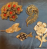 Set of 5 vintage gold-tone brooches laid out on clothing showing intricate details and designs.