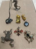 Seven costume jewelry pieces including animal-themed brooches and pendants displayed on beige background.