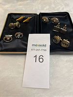Photo showing all six pairs of men's cufflinks arranged on black fabric, including gold and silver tones with various designs.