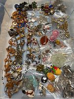 Overall view of the assorted vintage jewelry pieces in a box, showing necklaces, pins, and various loose items.