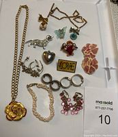 Photo showing the assortment of vintage jewelry items including necklaces, earrings, pins, and bracelets arranged on a white surface.