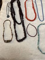 All necklaces laid out on a soft white surface showing different colors and bead types with the largest necklace measuring around 20 inches.