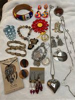 Photo showing assorted vintage jewelry collection with bracelets, earrings, brooches and necklaces with mixed materials including metal, beads, and wood.