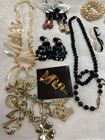 Full view of the 13 vintage jewelry items including necklaces, earrings, brooches, ring, and bracelet on flat surface