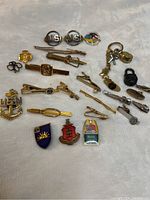 Overview of vintage men's cufflinks, tie clips, lapel pins in various gold and silver tones including nautical and military insignia.
