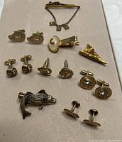 Overview of vintage men's cufflinks, tie clips, and lapel pins arranged on white surface