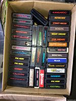 Overhead view of a cardboard box filled with Atari 2600 cartridges showing multiple titles across columns.