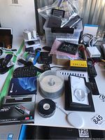 Full overview of assorted electronics on table: chargers, remotes, keyboard, DVD spindle, circuit boards in tote