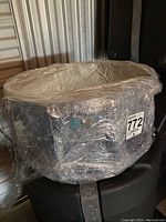 Side view of the plastic-wrapped Ludwig snare drum showing chrome shell and tension lugs