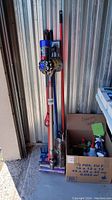 Dyson vacuum leaning against wall with long-handled tools and box of supplies