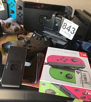 Front view showing Nintendo Switch dock, Joy-Con grip, Pro Controller, and boxed neon Joy-Con set.