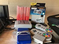 Overall view of SNES Classic mini console, two SNES controllers, NES Classic Mini controller in box, and a row of red-spined Switch game cases
