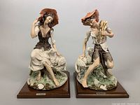 Front view of shepherd and shepherdess sculptures on wood bases, showing detailed porcelain figurines and name plaques.