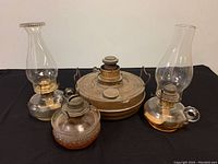 Four antique oil lamps, three with glass bases and one with brass base, including two glass chimneys.