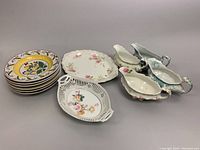 Overview of the lot showing stack of six Kellinghusen Trenk wall plates with colorful floral patterns, two decorated serving platters, and four gravy boats with floral details.