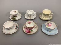 All six bone china teacup and saucer sets displayed from above, showing variety in floral patterns and gold trims.