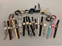 Photo showing entire collection of 22 assorted wristwatches laid out on a surface. Variety of straps including metal, leather, plastic, and fabric. Different styles including analog and digital watches.