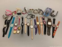 Full lot view of 23 assorted watches showing different sizes, strap colors and styles including leather, plastic, metal and rubber.