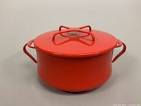 Front view of the vibrant orange Dansk enamel pot with lid, showing the rounded shape and integrated handles.