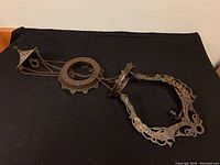 Full side view of the cast metal oil lamp holder showing chains and decorative frame