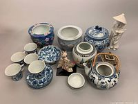 Photo showing 9-inch white ceramic Asian figurine, two floral planter pots, blue and white cups and saucers, two teapots, jars and additional decorative items.