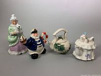 Four vintage ceramic decorative items displayed on table: Mamsellkanne watering can/jug figure, sailor-themed teapot, white leaf-decorated teapot, and cake-shaped cookie jar.