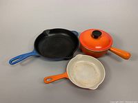 All three pieces visible: blue 10-inch skillet, orange 6-inch covered pot, and orange 7-inch skillet.