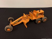 Side view of the vintage pressed steel toy road grader showing orange paint, six rubber tires, and 'Power Grader' decal on the arm.