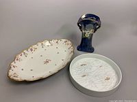 Photo showing all three items in the lot: the white Rosenthal round dish with water lily design, the Limoges oval scalloped platter with floral accents and gold trim, and the blue Maling vase with floral decoration.