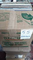 Sealed taped U-Haul box holding approx. 100 vinyl LPs, 12 inch size, stacked in storage.