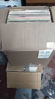 Large sealed cardboard box with approximately 100 vinyl albums, top edges showing album covers typical for 12-inch LPs.