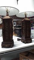 Pair of carved wooden Asian-style table lamps showing the front and base with dragon carving details and white lampshades.